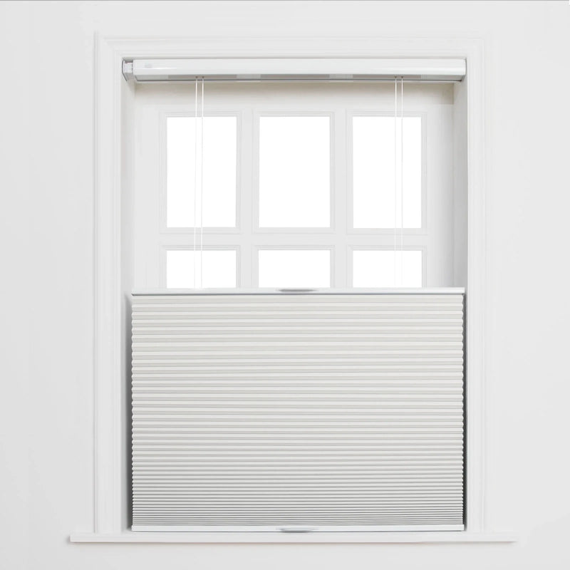 A white paneled window in an interior room featuring light grey top-down bottom-up cellular Blinds with sheer white pull strings and bright light through the upper panes