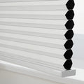 Digital photograph of a contemporary white cellular honeycomb Blind featuring visible black insulating cells and a sleek silver bottom rail resting on a pristine white window sill