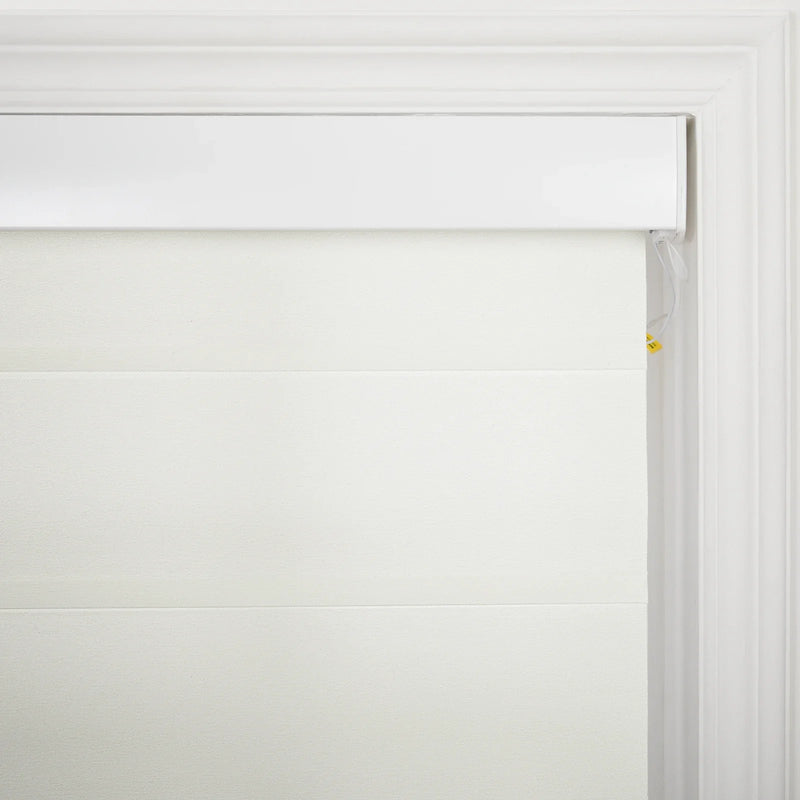 Photograph of a creamy white pleated window Blind with a textured fabric featuring a sleek white headrail and visible white control strings with a small yellow safety tag on the right, set against elegant white window molding