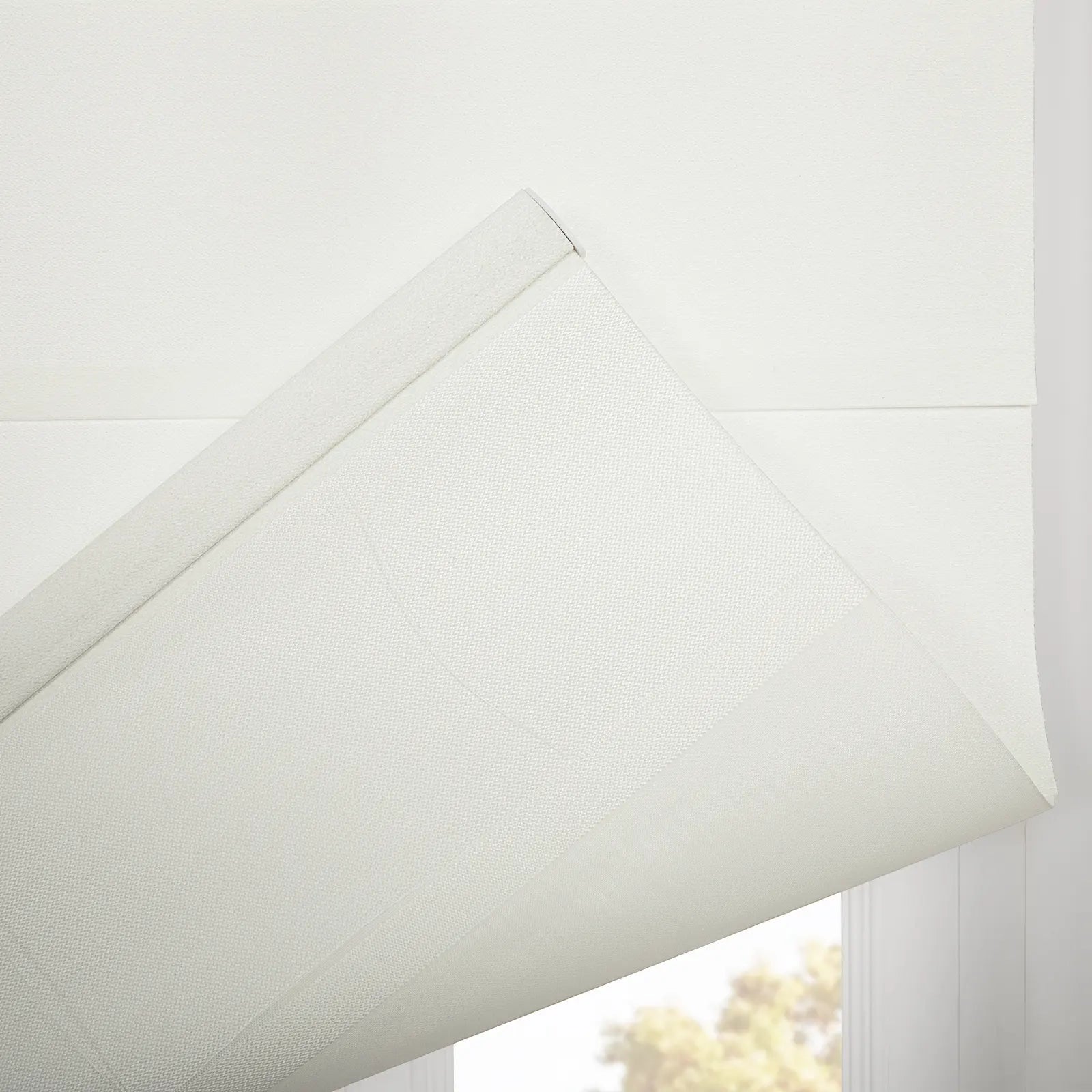 White textured Roman Blinds partially lowered over an interior window with a subtle geometric weave pattern and soft sunlight visible through outside trees