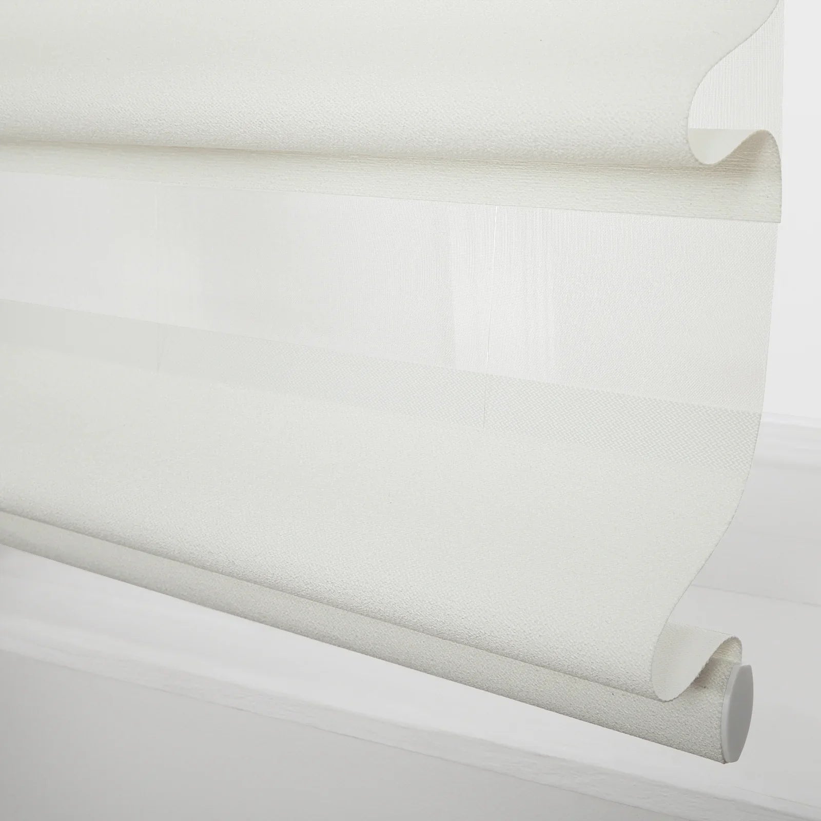 White layered roller Blind with alternating sheer and opaque textured fabric partially unrolled showing the bottom bar and end cap