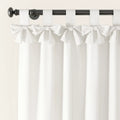 Close-up of elegant white linen-look curtains with bow-tied fabric loops hanging from a dark bronze curtain rod against a light wall