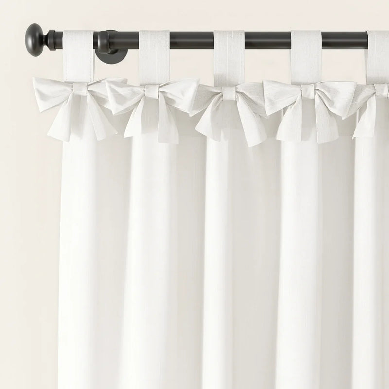 Close-up of elegant white linen-look curtains with bow-tied fabric loops hanging from a dark bronze curtain rod against a light wall