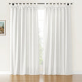 White linen texture curtains with decorative bow-tie tab tops hanging from a black rod in a sunlit room with hardwood floors, a visible outdoor green tree, and a small framed painting on the left wall