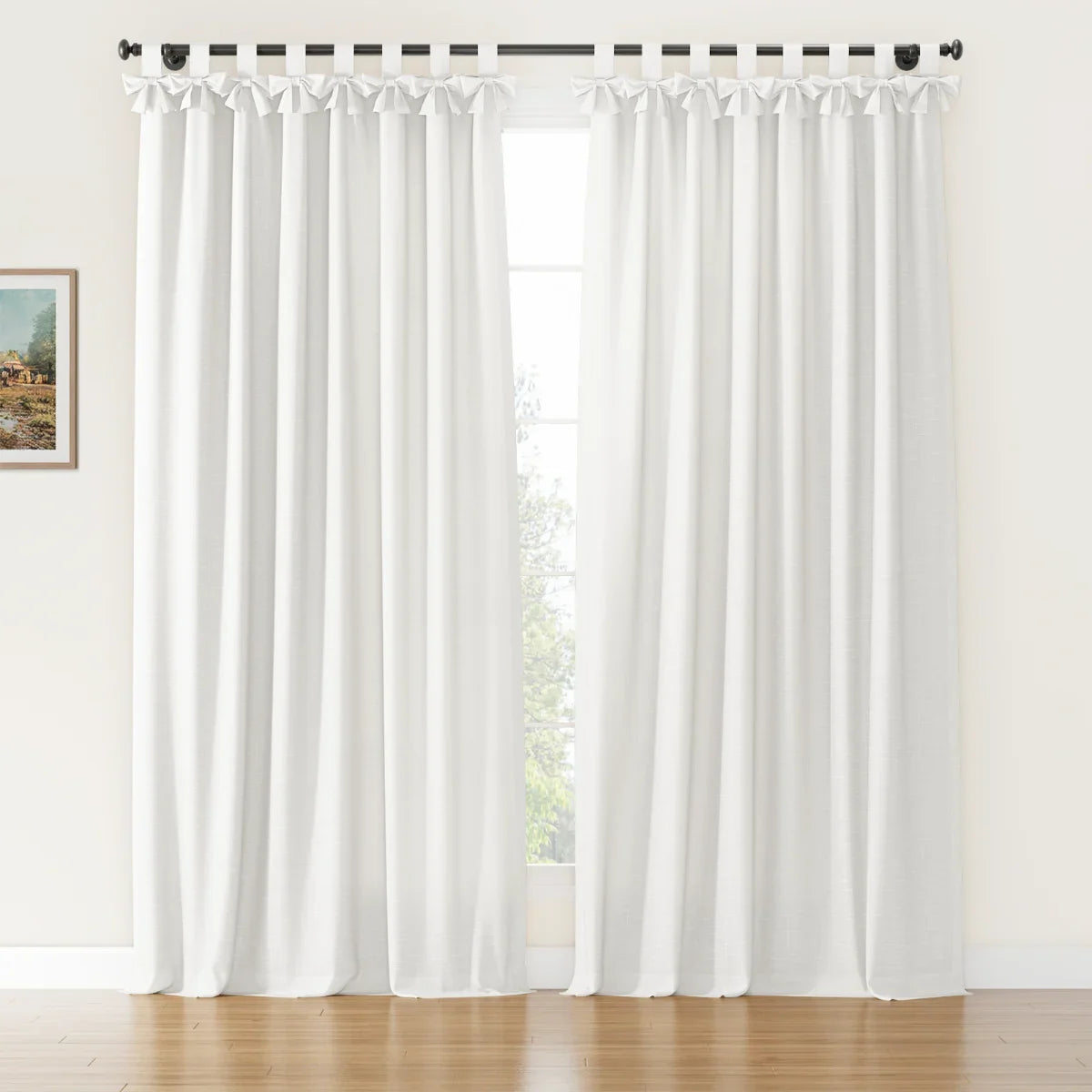 White linen texture curtains with decorative bow-tie tab tops hanging from a black rod in a sunlit room with hardwood floors, a visible outdoor green tree, and a small framed painting on the left wall