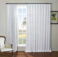 An interior room featuring a large window with white textured curtains, an elegant cream armchair with nailhead trim, and a framed botanical lemon print on the wall overlooking a sunny green field