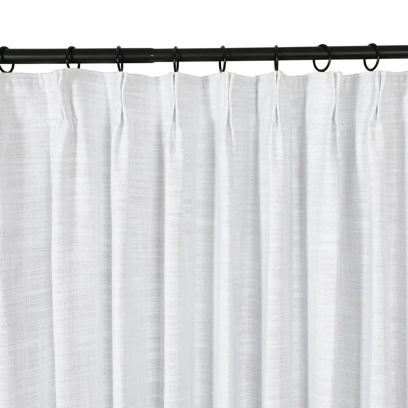 Photograph of white subtly textured curtains with a pleated header hanging on a black metal rod with rings