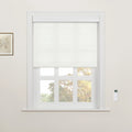 A room featuring a white framed window with partially lowered white Roman Blinds, showing autumn trees outside, complemented by a wall-mounted white remote control and a framed botanical art print