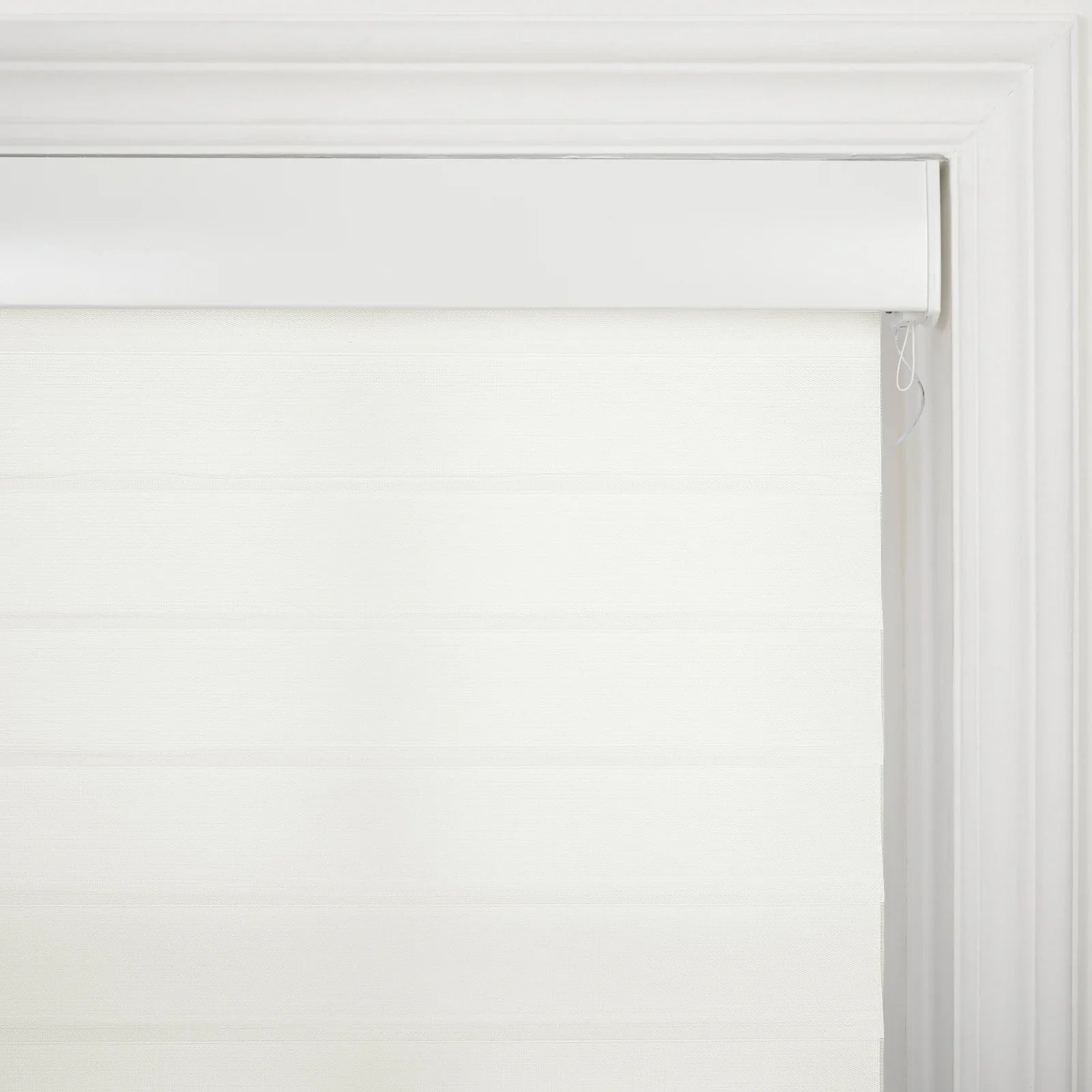 A white roller zebra Blind featuring alternating sheer and opaque horizontal stripes and a white valance, mounted within a decorative white window frame with a visible pull cord