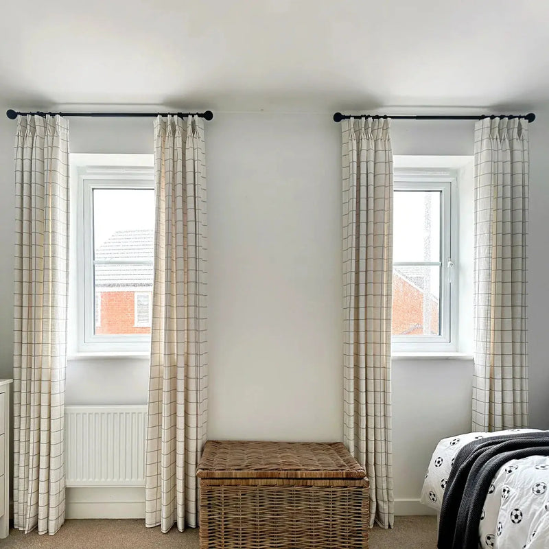 Photograph of a modern bedroom interior with two windows framed by cream checked curtains a woven wicker storage trunk and a bed featuring a soccer ball patterned duvet and dark grey throw
