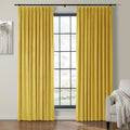 Bright yellow velvet pinch-pleated curtains frame a window with black grids in a modern living room featuring monochromatic tree art and a beige armchair with a textured white throw