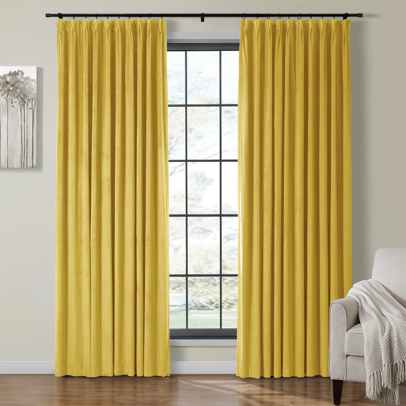 Bright yellow velvet pinch-pleated curtains frame a window with black grids in a modern living room featuring monochromatic tree art and a beige armchair with a textured white throw